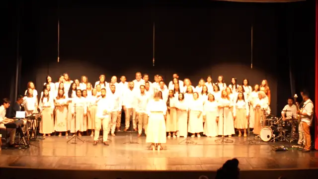 O Coral Uma Voz completo no palco, sob luz dourada